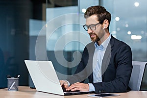 Successful mature businessman at work with laptop inside office, man in business suit sitting at desk typing on computer