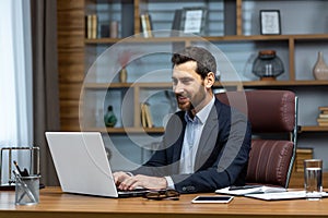 Successful mature businessman at work with laptop inside office, man in business suit sitting at desk typing on computer