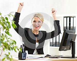 Successful middle-aged business woman holding arms up sitting at pc in office