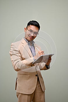 Successful millennial Asian businessman in formal business suit and glasses using his tablet
