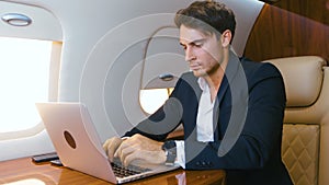 Successful millionere man wearing classical suit using laptop. Traveling in private jet plane. Businessman works at the