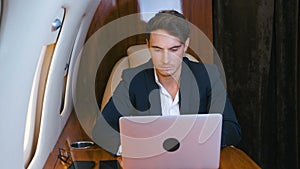 Successful millionere man wearing classical suit using laptop. Traveling in private jet plane. Businessman works at the