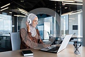 Successful modern businesswoman working inside office with laptop, Muslim woman wearing hijab and headphones listening