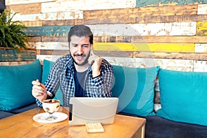 Successful modern middle age man freelancer talking on phone in cafe while using digital tablet and enjoying dessert in trendy