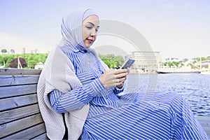 successful muslim woman looking at the phone on the river bank
