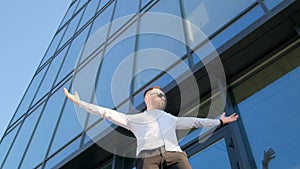 A successful office worker spreads his arms wide near a skyscraper in New York. A businessman from the USA