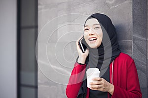 Successful operation. Arab businesswomen in hijab holding a coffee in the street and holding a cell phone