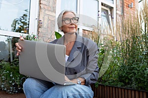 successful pretty middle aged woman dressed stylishly with laptop on cafe porch