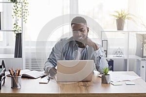 Successful project. Smiling businessman looking at laptop screen at workplace.