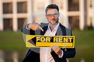 Successful real estate agent in a suit holding for rent sign near new apartment. Real estate agent with home loan