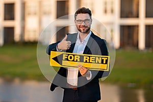 Successful real estate agent in a suit holding for rent sign near new apartment. Realtor or real estate agent shows