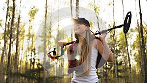 Successful search. Young woman holding metal detector in the forest. Direct sunlight