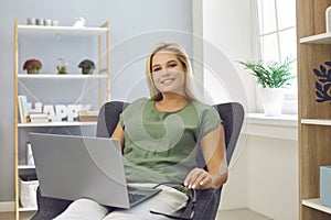 Successful self-made woman sitting in an armchair with laptop computer in her home office