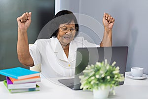 Successful senior woman working on laptop with arms raised