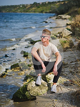 Handsome man sitting near water. A thoughtful guy on a blurred natural background. Male confidence concept. Copy space.