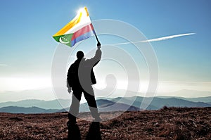 Successful silhouette man winner waving Comoros flag on top of the mountain