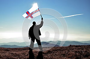 Successful silhouette man winner waving Faroe Islands flag on top of the mountain