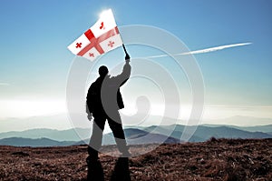 Successful silhouette man winner waving Georgian flag on top of the mountain