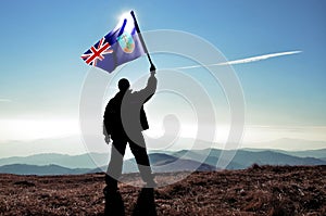 Successful silhouette man winner waving Montserrat flag on top of the mountain