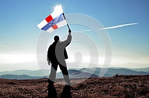 Successful silhouette man winner waving Netherlands Antillesflag on top of the mountain