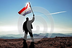 Successful silhouette man winner waving Netherlands flag on top of the mountain