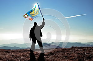 Successful silhouette man winner waving Pierre and Miquelon flag on top of the mountain