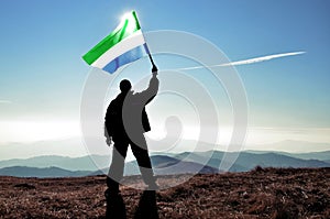 Successful silhouette man winner waving Sierra Leone flag on top of the mountain