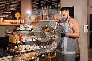 Successful small business owner in cafe using digital tablet and looking at screen. Serious barista with a beard