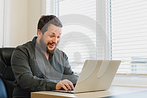 Successful smiling broker sitting at office with laptop near window.