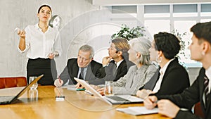 Successful smiling young businesswoman explaining new business strategy to partners sitting at table in office