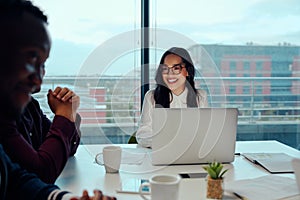 Successful smiling young woman sitting with his multiethnic colleagues at a corporate business meeting