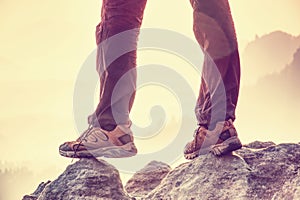 Successful sports man hiker legs standing on mountain top. Outdoor trousers and trekking leather boots. Trail in misty valley