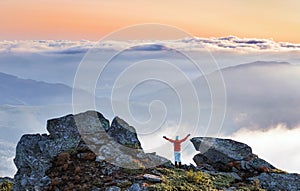 Successful sporty girl is standing at the edge of the precipice. Mountains landscape in the foggy morning. Sunrise. Autumn