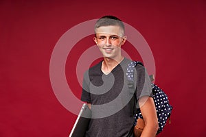 Successful student with a backpack and laptop in hand on a red background