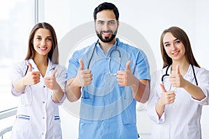 Successful team of medical doctors are looking at camera and smiling while standing in hospital