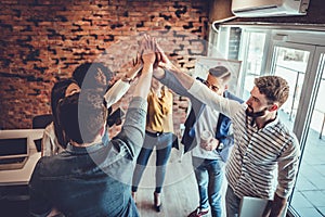 Successful team of young professionals celebrating achievement in work project giving high-five to each other in office