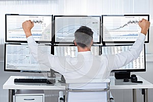 Successful Trader With Arms Raised Looking At Graphs On Screens