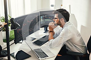 Successful trader. Back view of bearded stock market broker in eyeglasses analyzing data and graphs on multiple computer