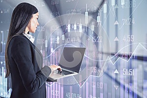 Successful trader concept with young woman with laptop in front of digital screen with financial chart graphs and quotes