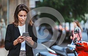 Successful woman in business suit holds sellphone in hand pays for online app scooter rental for trip around barcelona