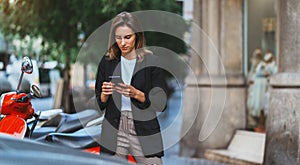Successful woman in business suit holds smartphone in hand pays for online scooter rental for quick trip around city barcelona