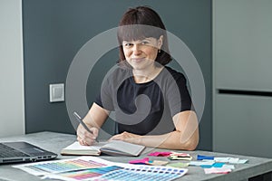 Successful woman plans work schedule, writes in notebook, sitting at workplace with laptop