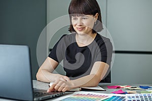 Successful woman plans work schedule, writes in notebook, sitting at workplace with laptop