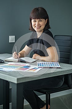 Successful woman plans work schedule, writes in notebook, sitting at workplace with laptop