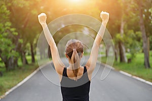 Successful woman raising arms after cross track running on summer sunset. Fitness female athlete with arms up celebrating success