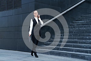 Successful woman talking on mobile phone, holding laptop on background steps