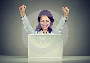 Successful woman winner with arms raised looking at laptop