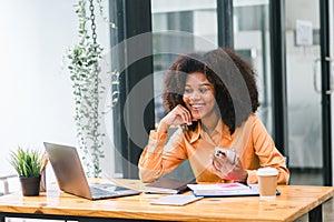 Successful young African American pretty woman, entrepreneur in casual wear, smiling, working on laptop in a modern