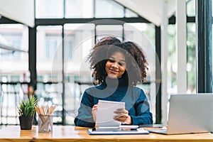 Successful young African American pretty woman, entrepreneur in casual wear, smiling, working on laptop in a modern