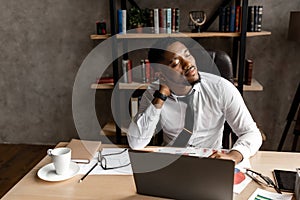 Successful young african businessman tired to sit at his desk in the office, working on laptop